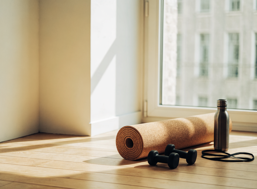 Esterilla, mancuernas y botella listas para entrenar junto a una ventana